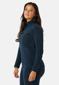 Marineblauwe fleece pullover met hoge kraag, ritssluiting, gestructureerde stof en een getailleerd ontwerp. Kenmerkt subtiele zijnaden en een logodetail.