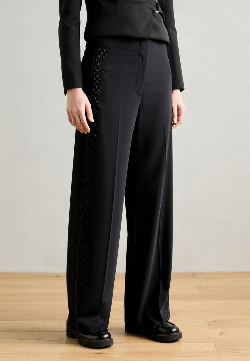 Black wide-leg trousers with a smooth texture, featuring vertical rhinestone accents along the pockets and a tailored fit.
