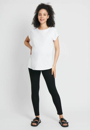 Top bianco a maniche corte abbinato a leggings neri e sandali neri. Il top presenta un collo rotondo e una vestibilità comoda.