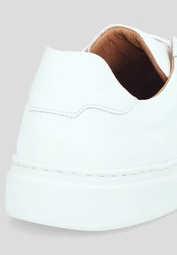 Białe skórzane trampki o gładkiej fakturze, zaokrąglonym kształcie, widocznych szwach i niskoprofilowej podeszwie. Wnętrze wykonane jest z brązowej skóry.