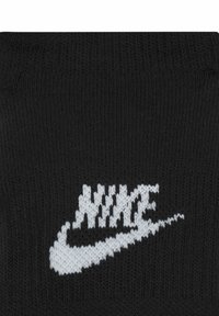 Calzino nero realizzato in tessuto lavorato a maglia con il logo Nike bianco in evidenza. La texture appare liscia con un motivo uniforme.