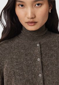 Hnedý, textúrovaný rolákový sveter s zapínaním na gombíky. Má štyri svetlé gombíky a mäkký, príjemný vzhľad.