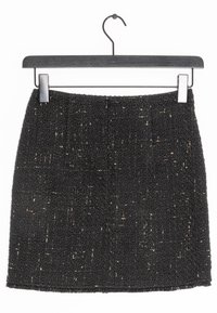 Jupe en tweed noir sur un cintre noir avec des accents métalliques. Elle présente une surface texturée et une coupe droite avec une taille.