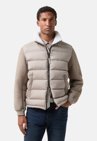 Pufferjakke i beige med lynlås foran, kunstpelskrave og glat stof med et dunfyldt design. Båret over en skjorte med krave.