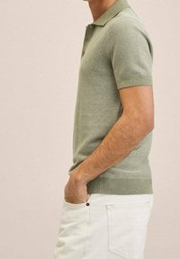 Polo à manches courtes vert clair, en maille texturée avec des rayures subtiles, col et ourlet côtelés, associé à un pantalon blanc.