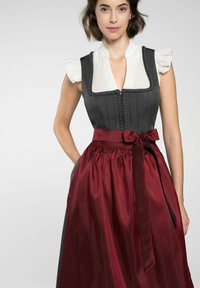 Traditioneel dirndl-jurk met een donkergrijze lijfje, een witte gerimpelde blouse en een bordeauxrok. Kenmerkt zich door ingewikkelde stiksels en een gestrikte taille.