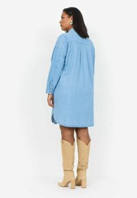 Zils džinsu krekls kleita ar garām piedurknēm, pogu detaļām, sānu šķēlumiem un izliekto apakšmalu. Pārdēvēta ar bēšiem līdz ceļiem augstiem zābakiem.