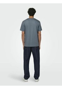 T-shirt in cotone grigio con maniche corte, scollo rotondo e vestibilità relax, abbinato a jeans in denim scuro e sneakers bianche.