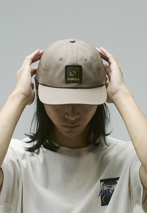 Brown baseball cap with a flat brim, featuring a square black patch embossed with a yellow rocket graphic and the word "FORMER."
