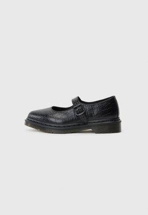 Zapato tipo Mary Jane negro con cuero estampado de cocodrilo, hebilla ajustable y suela gruesa de goma sobre un fondo gris claro.
