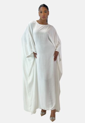 Abito maxi bianco realizzato in tessuto leggero con maniche fluide, vestibilità ampia e trama morbida. Accentuato da scarpe col tacco beige.