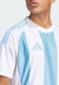 T-shirt de sport blanc avec des rayures verticales bleu clair, doté d'un tissu texturé, d'un col rond et du logo Adidas sur la poitrine.