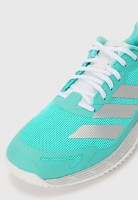 Türkise Laufschuhe mit einem atmungsaktiven Mesh-Obermaterial, weißen Schnürsenkeln, silbernen Akzenten an der Seite und einer strukturierten Gummisohle.