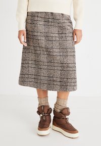 Skjørt i ullblanding med rutemønster i brunt og svart, kne-langt, sammen med brune isolerte støvler og beige strikkede sokker.