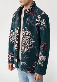 Minkštas džemperis mėlynos spalvos su baltais ir burgundiškių gėlių raštais. Su užtrauktuku ir aukštu apykakle. Minkšta tekstūra, laisvas kirpimas.