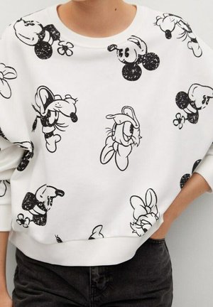 Sweat-shirt blanc avec des croquis répétés en noir et blanc des personnages classiques de souris et de canard de dessin animé, porté avec un pantalon sombre.