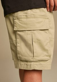 Beige cargo shorts med to store sidelommer, lavet af letvægtsstof. Har syningsdetaljer og en lige benæd.