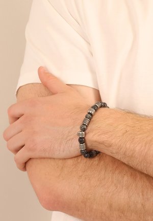 Bracelet made of black beads with silver-tone accents. Features a mix of matte and shiny finishes, showcasing intricate detailing between beads.