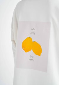 Witte oversized sweatshirt met een grafisch druk van twee gele citroenen en de tekst "easy peasy lemon squeezy" in het groen gedrukt.