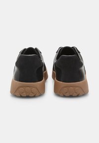 Svarta sneakers med en slät läderöverdel och mockadetaljer. Utrustade med en kraftig brun gummisula med cirkulära gripmönster.