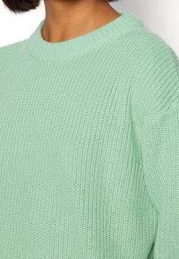 Maglione in verde menta lavorato a maglia con una texture a coste larga e un collo arrotondato. Le maniche sono leggermente scese, evidenziando un fit rilassato.