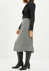 Blazer negro corto con mangas largas, combinado con una falda midi de cuadros en blanco y negro y botas de tacón negras hasta la rodilla.