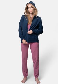 Felpa con zip blu navy e cappuccio, abbinata a pantaloni lunghi rosa. La felpa presenta una zip frontale e polsini a costine; tessuto morbido e casual.