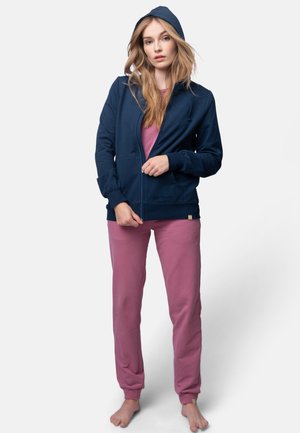 Marine blauwe hoodie met rits en capuchon, gecombineerd met roze lange broeken. De hoodie heeft een voorkeursrits en ribgebreide boorden; gemaakt van zachte, casual stof.