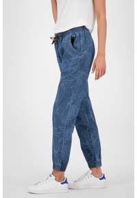 Blaue gemusterte Jogginghosen mit einem elastischen Bund, Kordelzug und gerippten Knöcheln. Kombiniert mit weißen Sneakern mit blauen Akzenten.