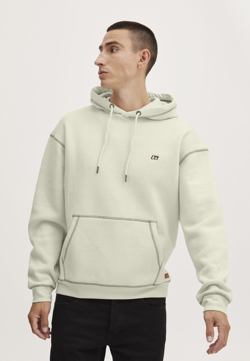 Sudadera verde claro hecha de una tela suave, con un bolsillo frontal, capucha con cordón y costuras en contraste. Logo pequeño en el pecho.