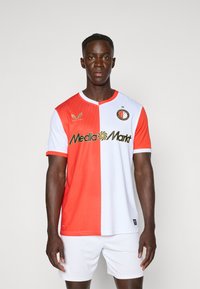 Fußballtrikot in roten und weißen Hälften mit einem strukturierten Muster. Verfügt über einen runden Halsausschnitt und kurze Ärmel, geschmückt mit einem Logo und goldenem Text.