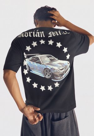 Personne portant un t-shirt noir avec un motif de voiture de sport argentée et des étoiles disposées en cercle dans le dos.