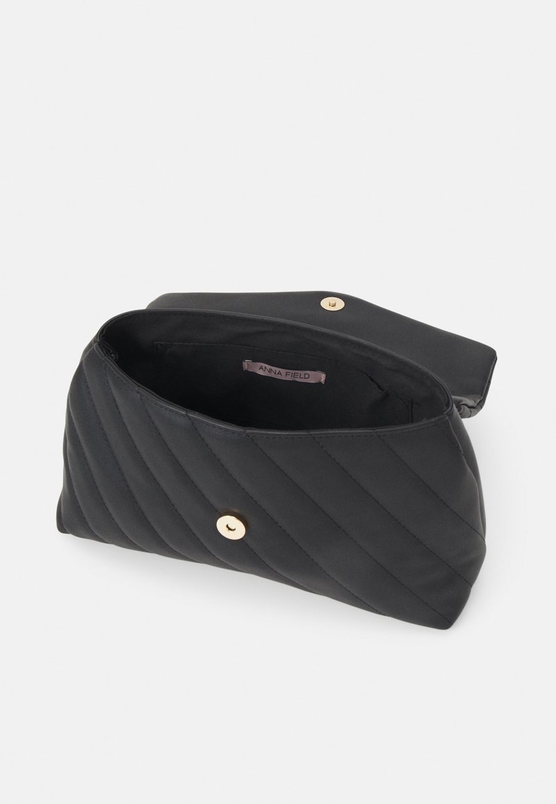 Sac à main noir matelassé avec une fermeture à bouton doré, ouvert pour montrer la doublure intérieure en tissu et une petite étiquette indiquant "Anna Field."