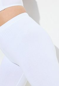 Bílé legíny z měkké, elastické látky s elastickým pasem. Povrch je hladký a střih těsně kopíruje tvar těla.