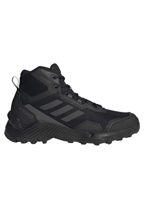Chaussure de randonnée noire mi-haute avec semelle texturée, cheville rembourrée, lacets et trois bandes sur le côté pour une utilisation en extérieur et sur sentiers.