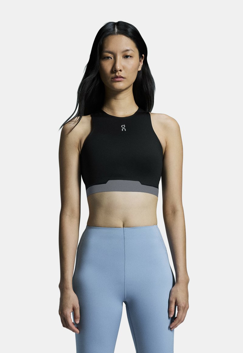Black sports bra with a high neckline and gray band. Made of stretchy material, featuring a logo on the chest and a sleek design.