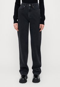 Kõrgelt vöödiga mustad denim püksid, mis omavad lõdva sobivust, viit taskut ja silmapaistvaid õmblusaktsente, millele on pandud juurde massiivsed mustad saapad.