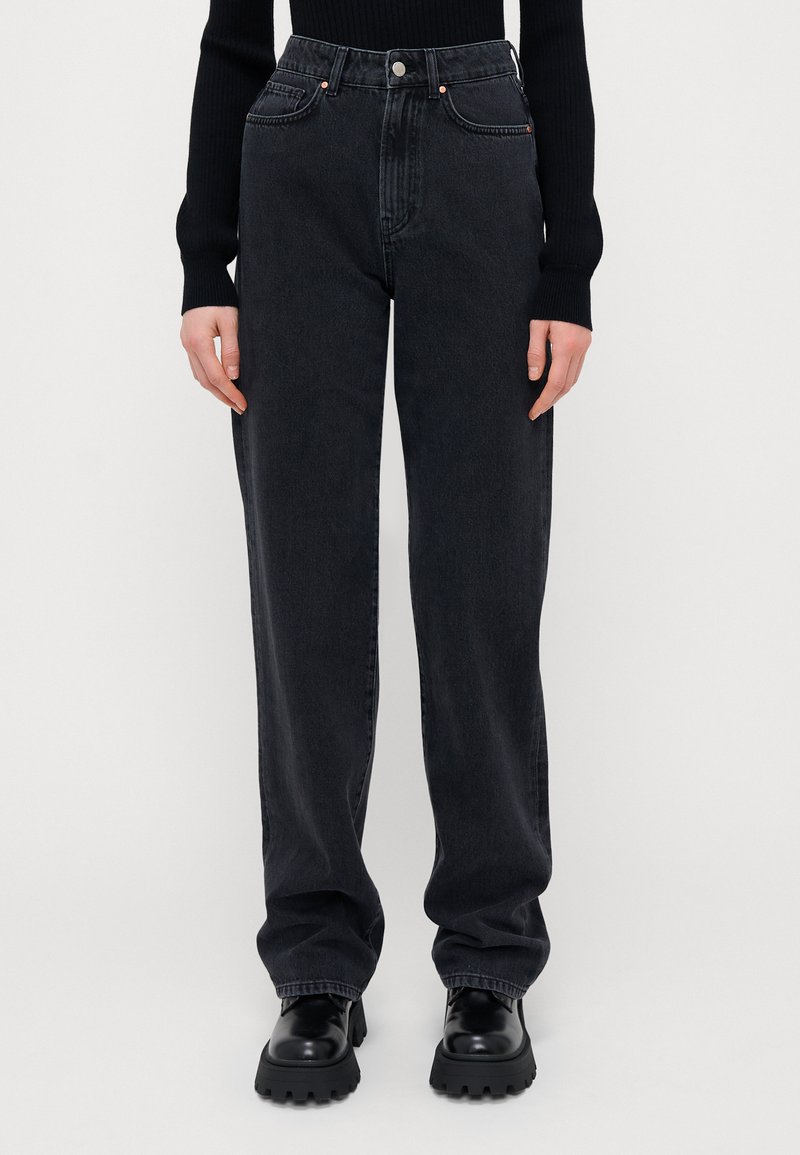 Kõrgelt vöödiga mustad denim püksid, mis omavad lõdva sobivust, viit taskut ja silmapaistvaid õmblusaktsente, millele on pandud juurde massiivsed mustad saapad.