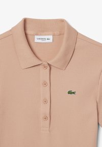 Vaaleanpunainen ribbipaita klassisella kauluksella, neljän napin nappilistalla ja vihreällä brodeeratulla Lacoste-logolla vasemmassa rinnassa.