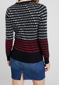 Sweter wykonany na drutach z czarnym tłem, na którym powtarza się biało-czerwony napis „MAISON SCOTCH”, ozdobiony gwiazdkami. Połączony z dżinsową spódnicą.
