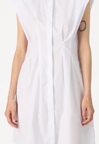 Λευκό, κοντομάνικο φόρεμα πουκαμίσα με κουμπιά στο μπροστινό μέρος, διακοσμημένο με πτυχώσεις και χαλαρή εφαρμογή. Λείος ύφασμα με ελαφριά γυαλάδα.