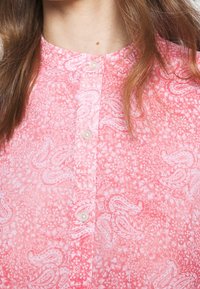 Chemise rose à boutons avec un motif cachemire et un tissu texturé. La chemise possède un col arrondi et des boutons translucides.