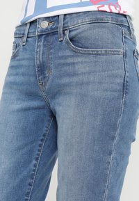 Vaqueros de mezclilla azul claro con un diseño clásico de cinco bolsillos, sutiles desgaste en la tela y un botón de metal en la cintura.