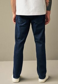 Jeans din denim de culoare albastru închis, cu un design drept, dotate cu două buzunare pe spate și purtate cu teniși albi. Textură moale, tăietură obișnuită.
