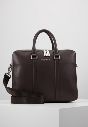 Mallette en cuir Valentino brun foncé avec double poignée, tirettes de fermeture éclair argentées et bandoulière détachable reposant sur un socle blanc.