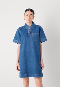 Denimkjole i blått med krage, korte ermer, brystlomme med sømdetaljer og rett kant.