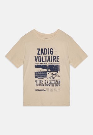 Camiseta de algodón beige con mangas cortas que presenta texto gráfico azul e imágenes relacionadas con una gira de conciertos, con un corte relajado.