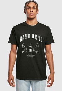 Must musta T-särk, millel on julge valge "GANG GANG" tekst ja graafilised kujundid. Lühikesed varrukad, ümar kaelus ja standardne istuvus.