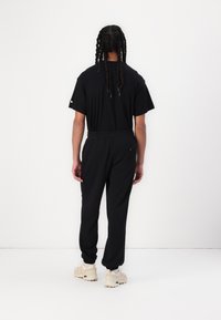 Zwarte t-shirt en bijpassende joggingbroek met een elastische tailleband. De joggingbroek heeft een achterzak en geribbelde boorden. G draagt het met lichte sneakers.