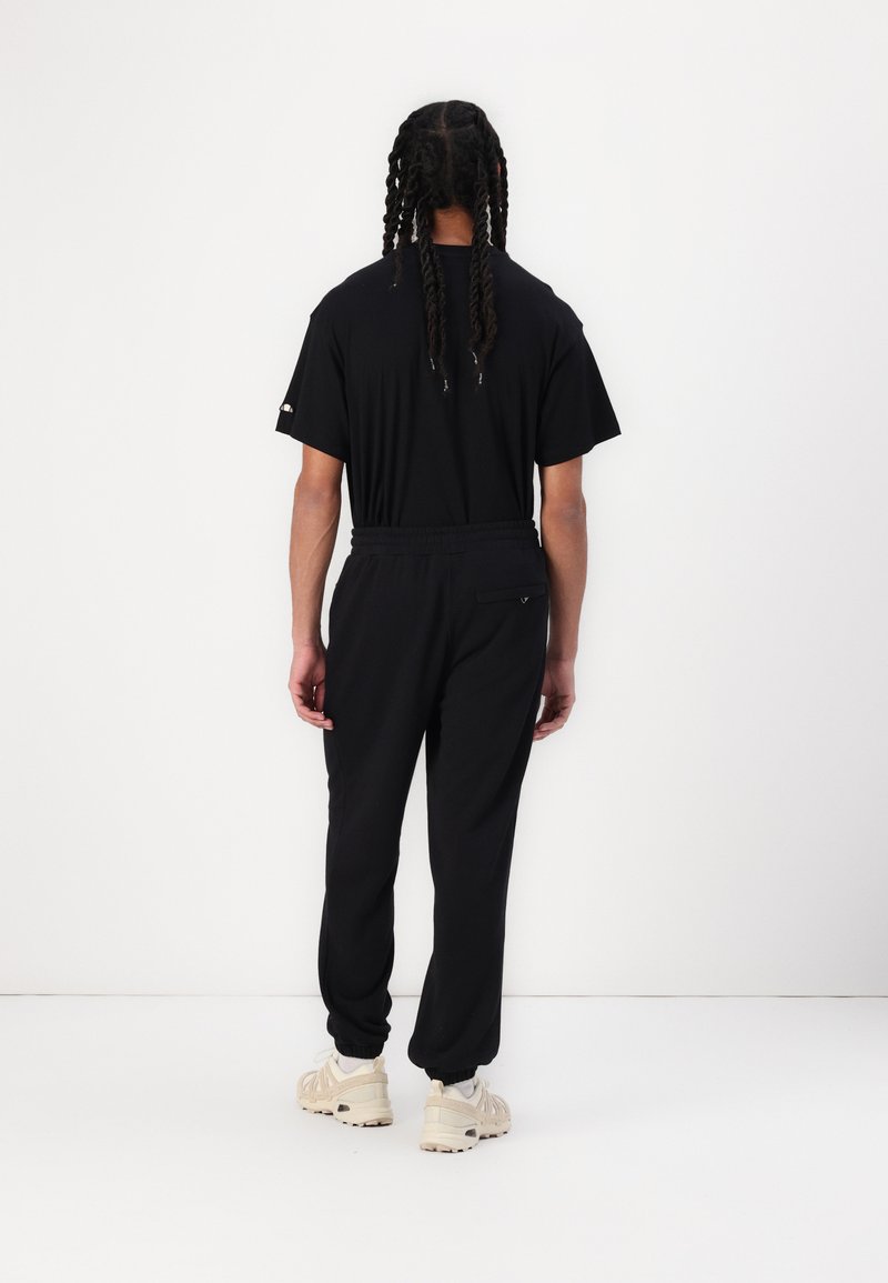 Czarna koszulka i dopasowane joggery z elastycznym paskiem. Joggery mają tylnią kieszeń i prążkowane mankiety. Noszone z jasnymi sneakersami.